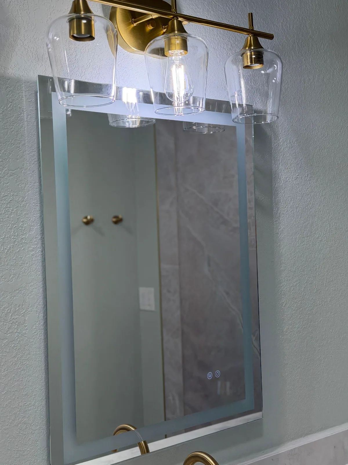 Backlit LED bathroom mirror under a brushed gold vanity light bar