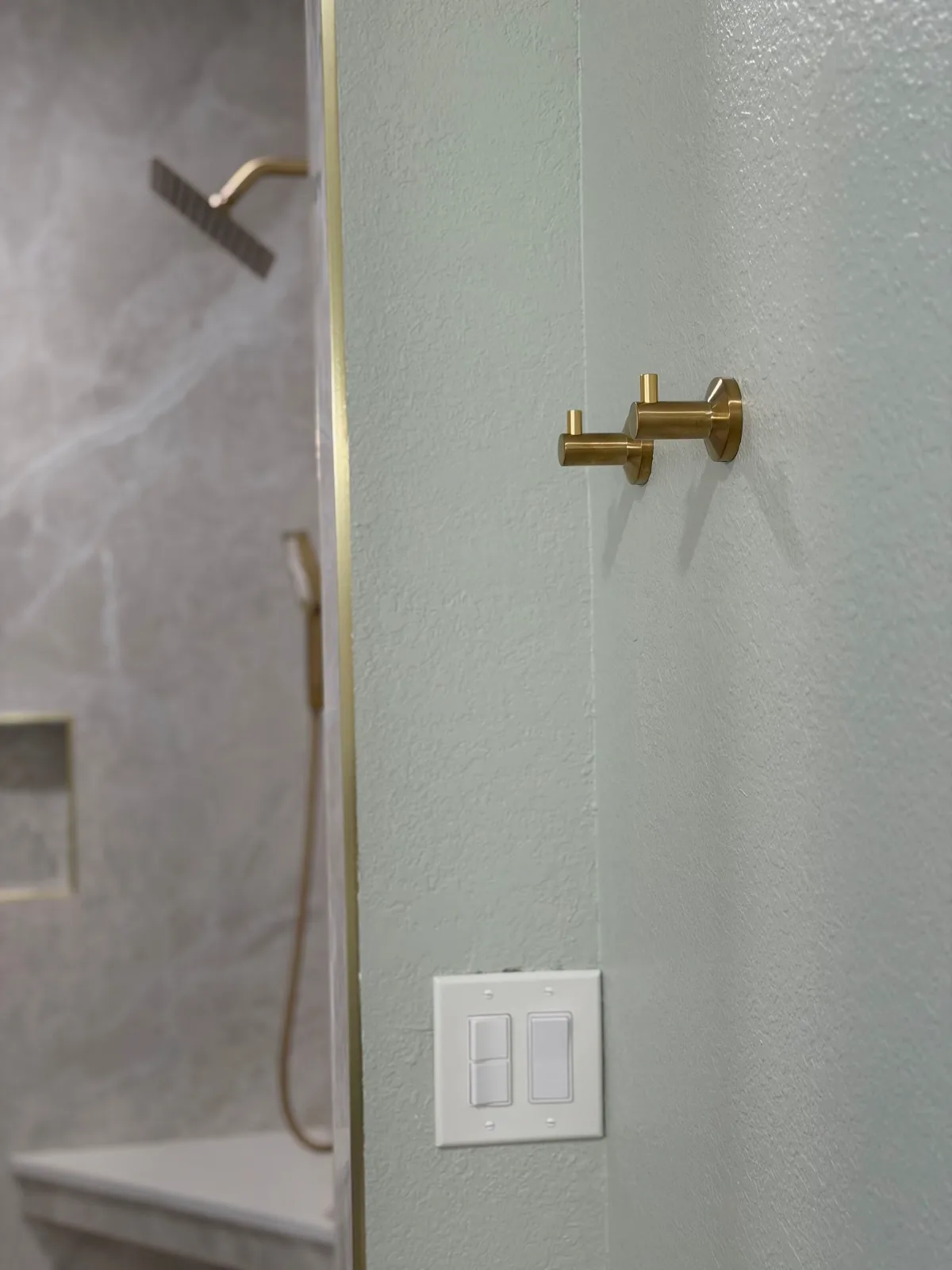 Brushed gold shower valve and diverter set into large-format marble-look porcelain