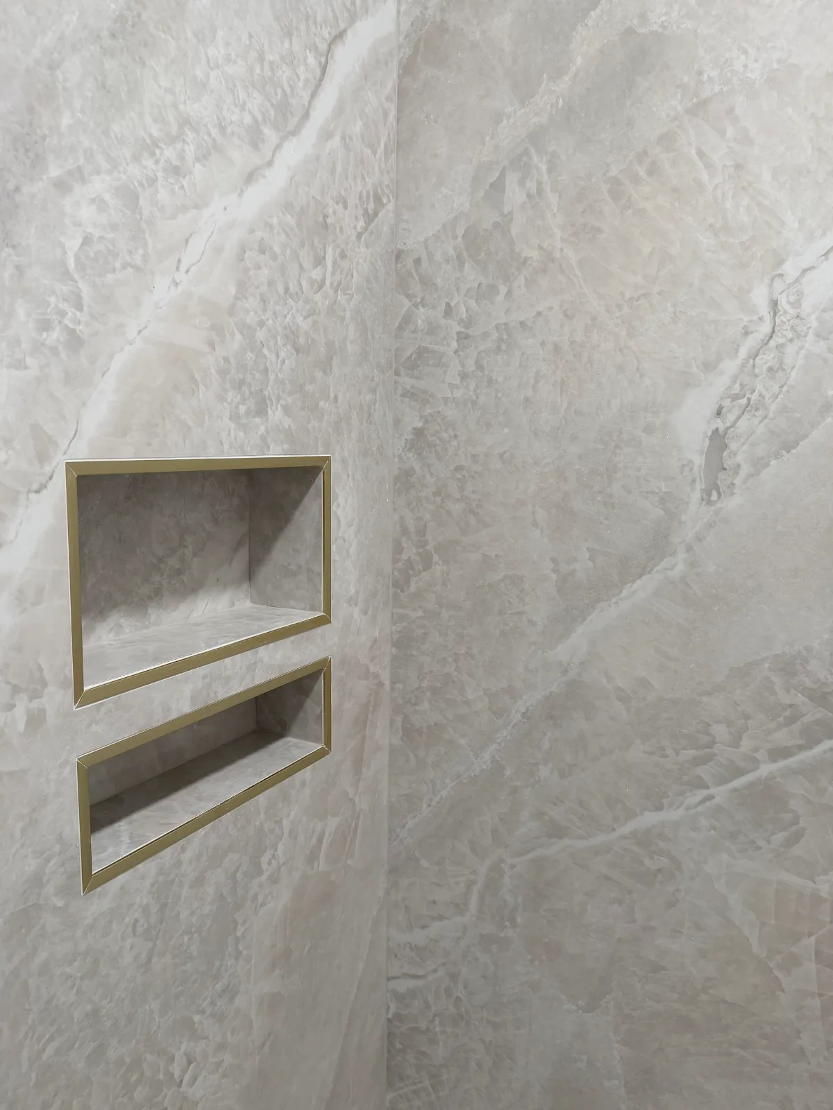 Two stacked recessed shower niches trimmed in brushed gold on marble-look porcelain