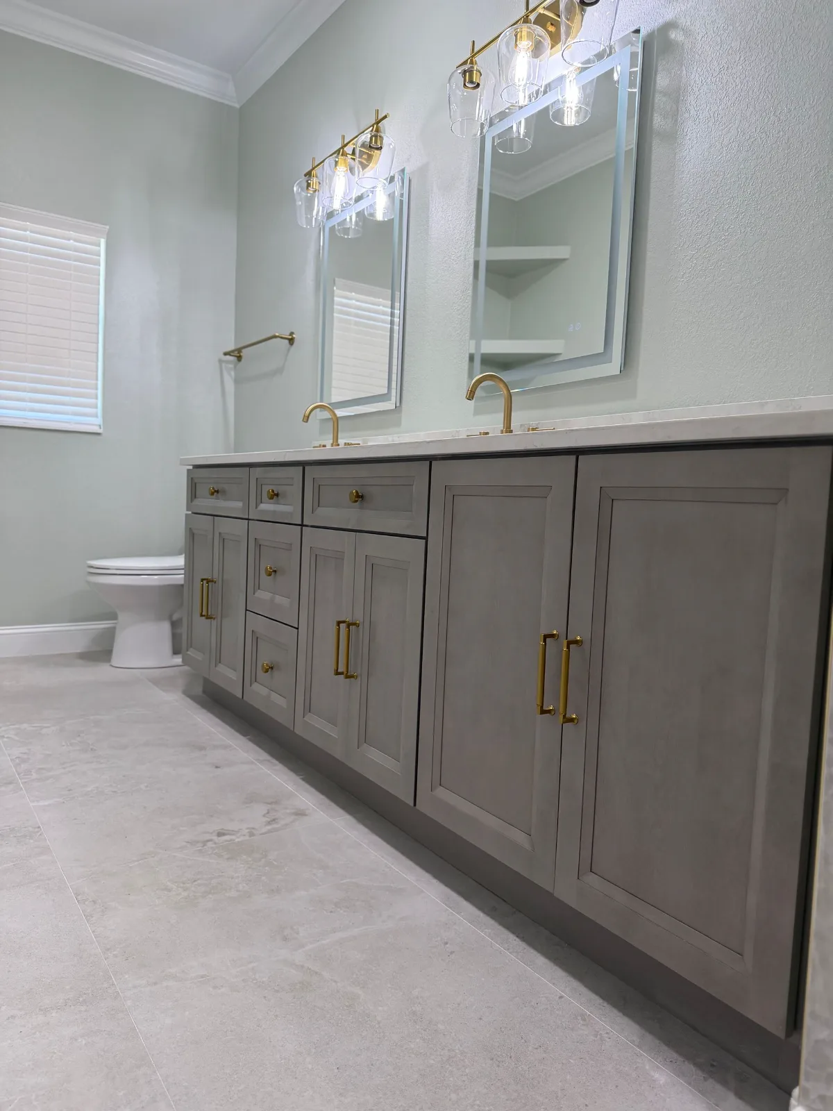 Gray shaker double vanity with brushed gold hardware and backlit LED mirrors