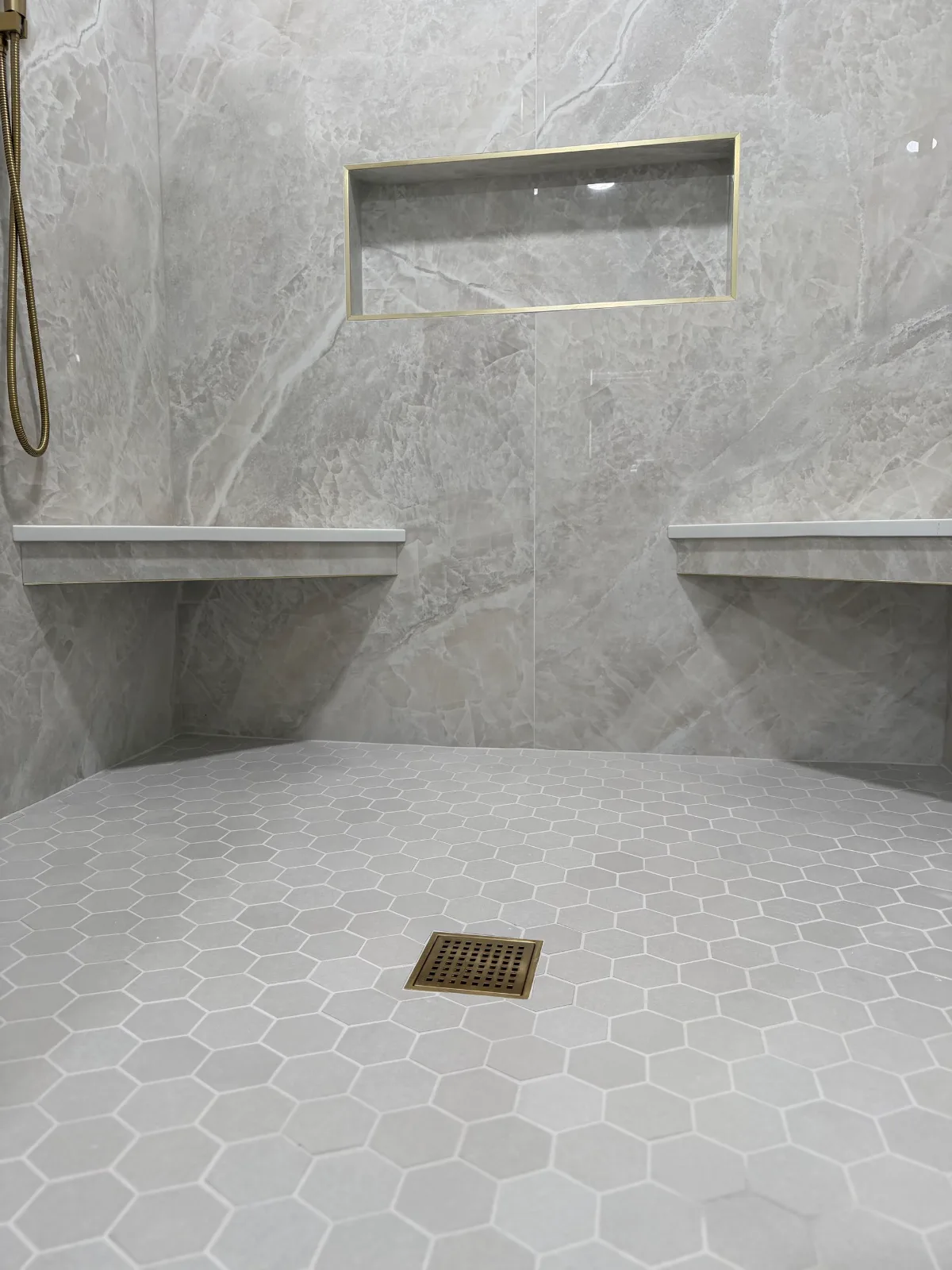 White hexagon mosaic shower floor with brushed gold square drain and quartz benches