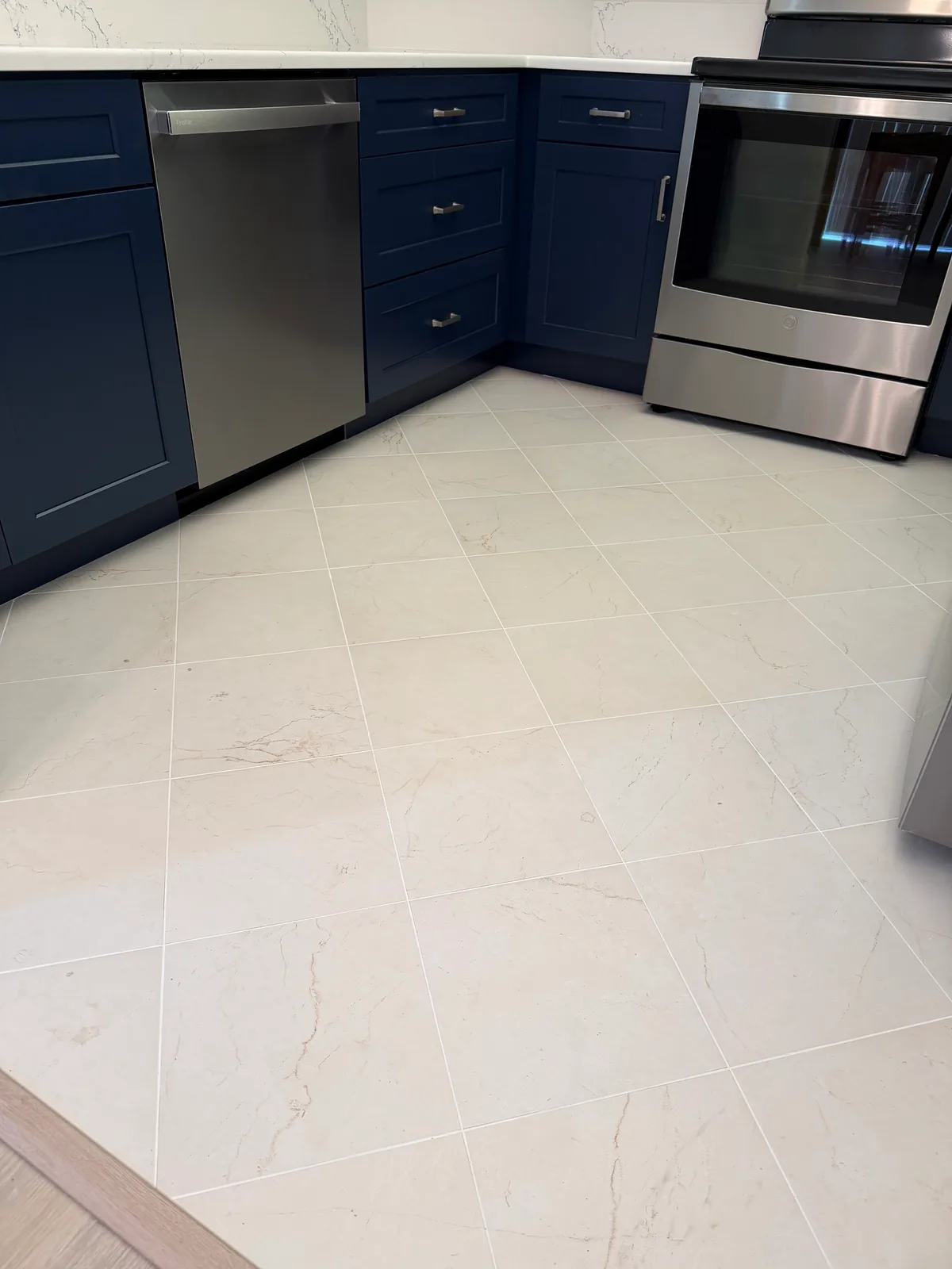 Large-format tile flooring laid through a kitchen with navy shaker cabinetry
