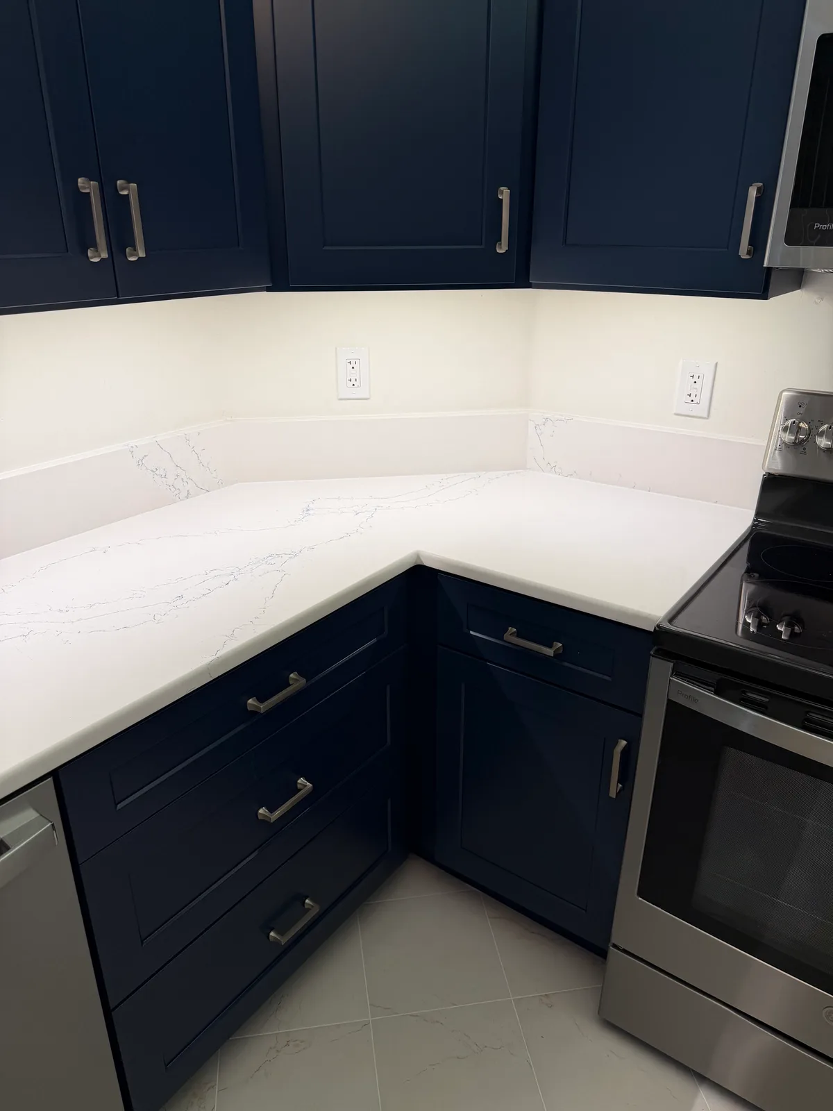 Navy shaker uppers with brushed hardware over a veined quartz counter