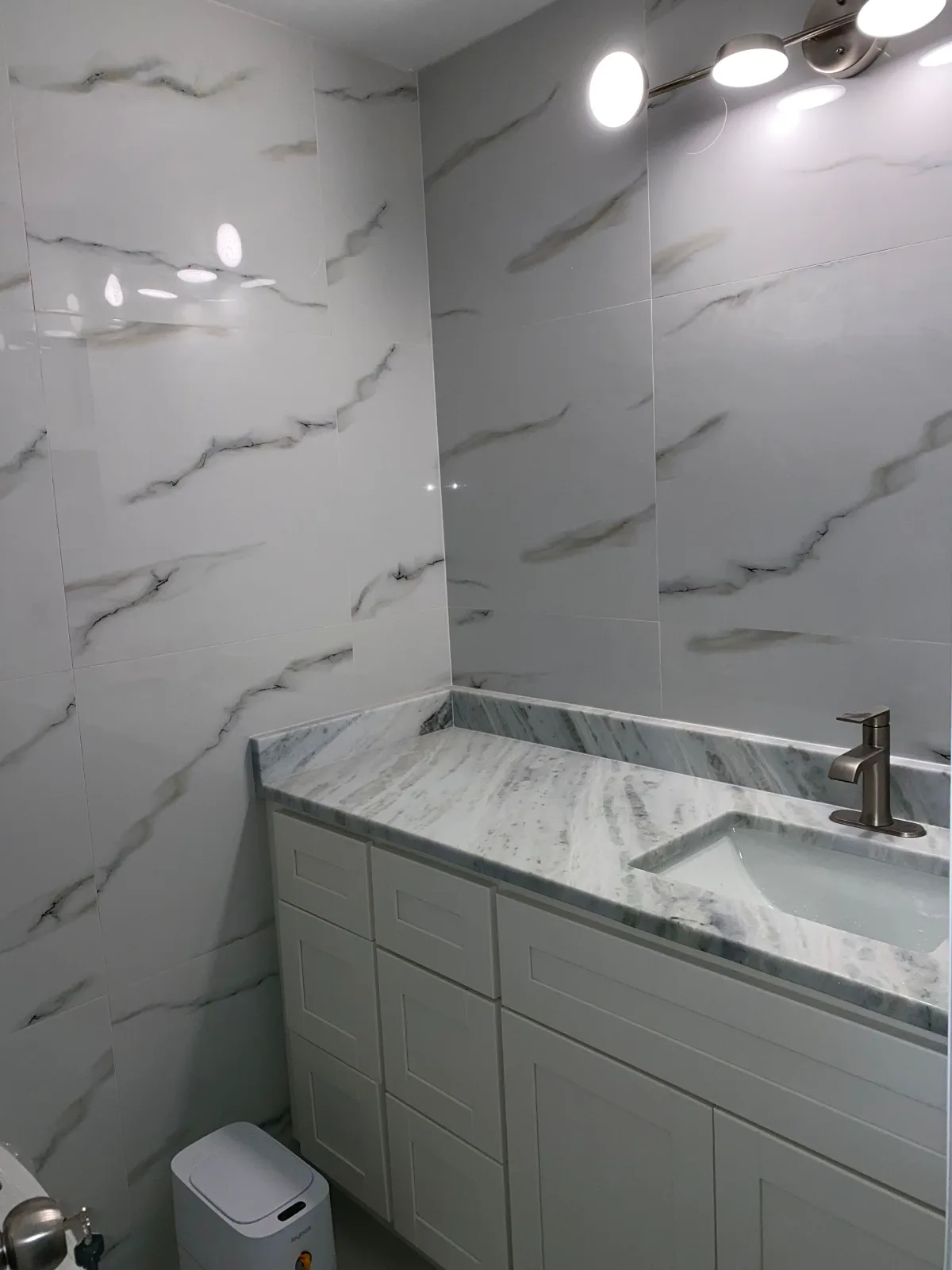 Gray vanity with granite top against a marble-look tile wall