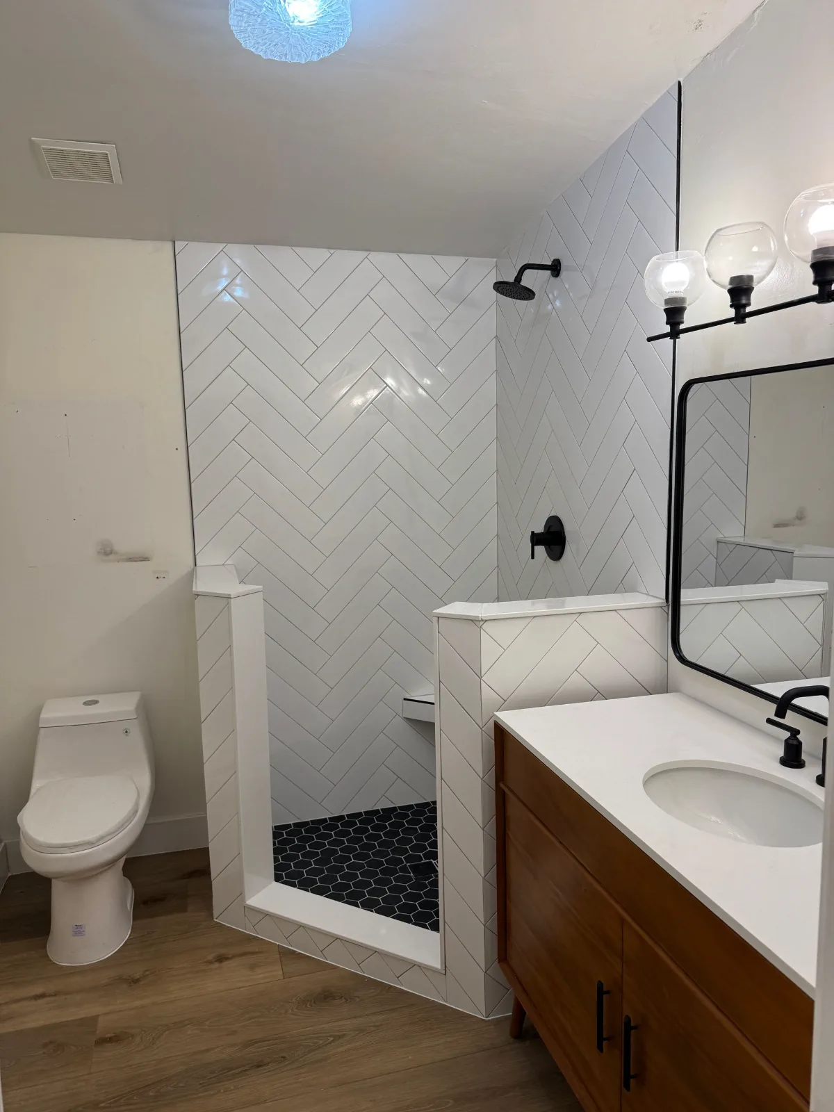 Herringbone tile shower with black pebble floor and a wood vanity