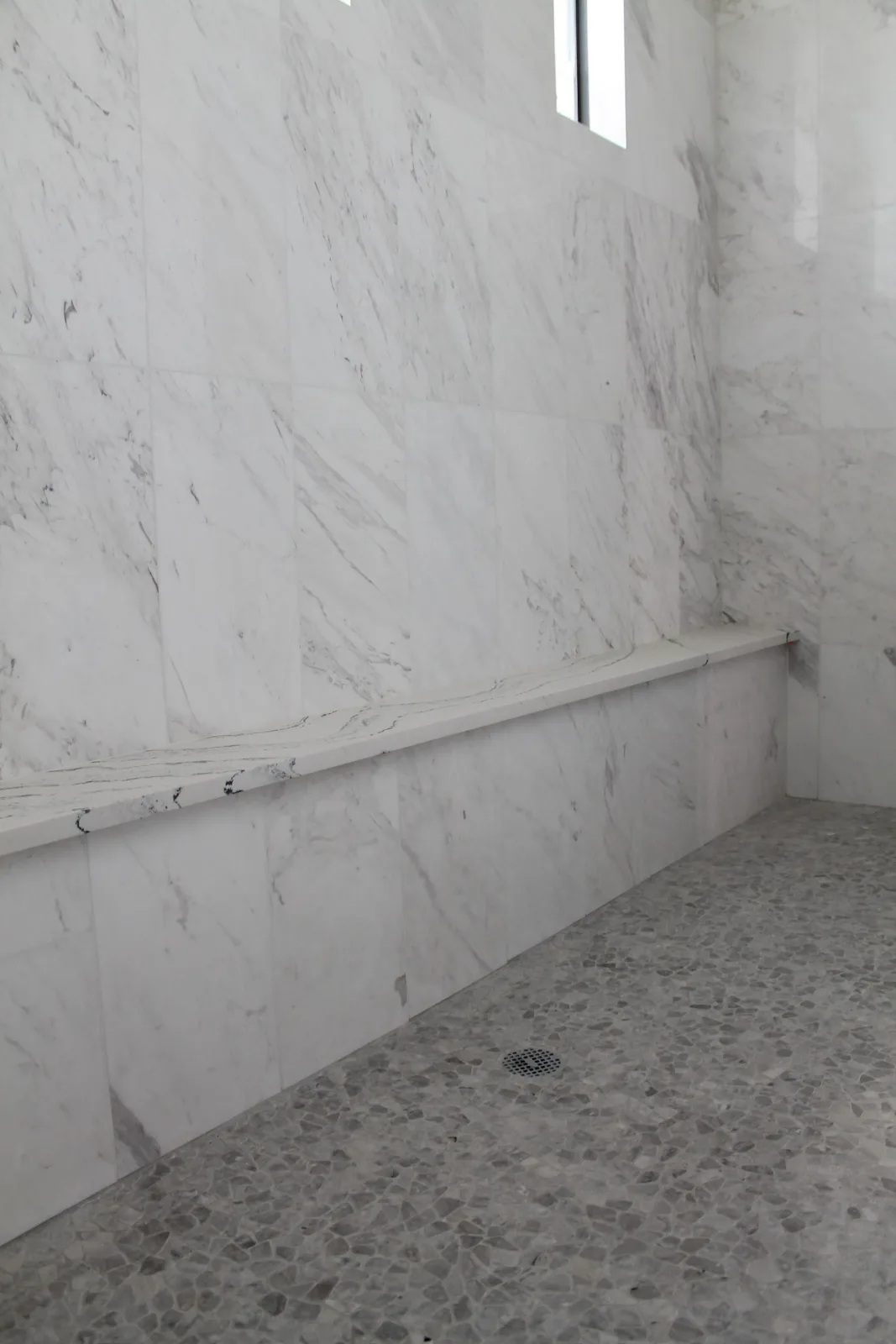 Marble-look porcelain shower with a full-length quartz bench