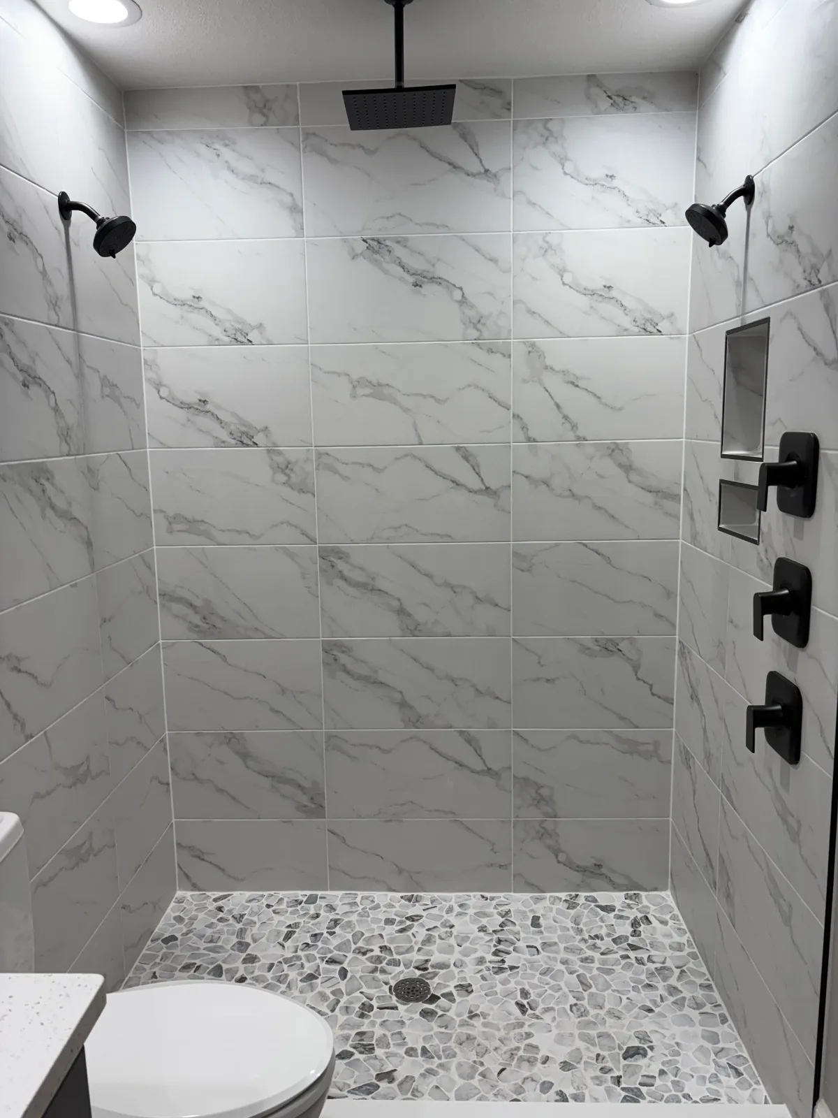 Matte black thermostatic valves and body jets on marble-look tile