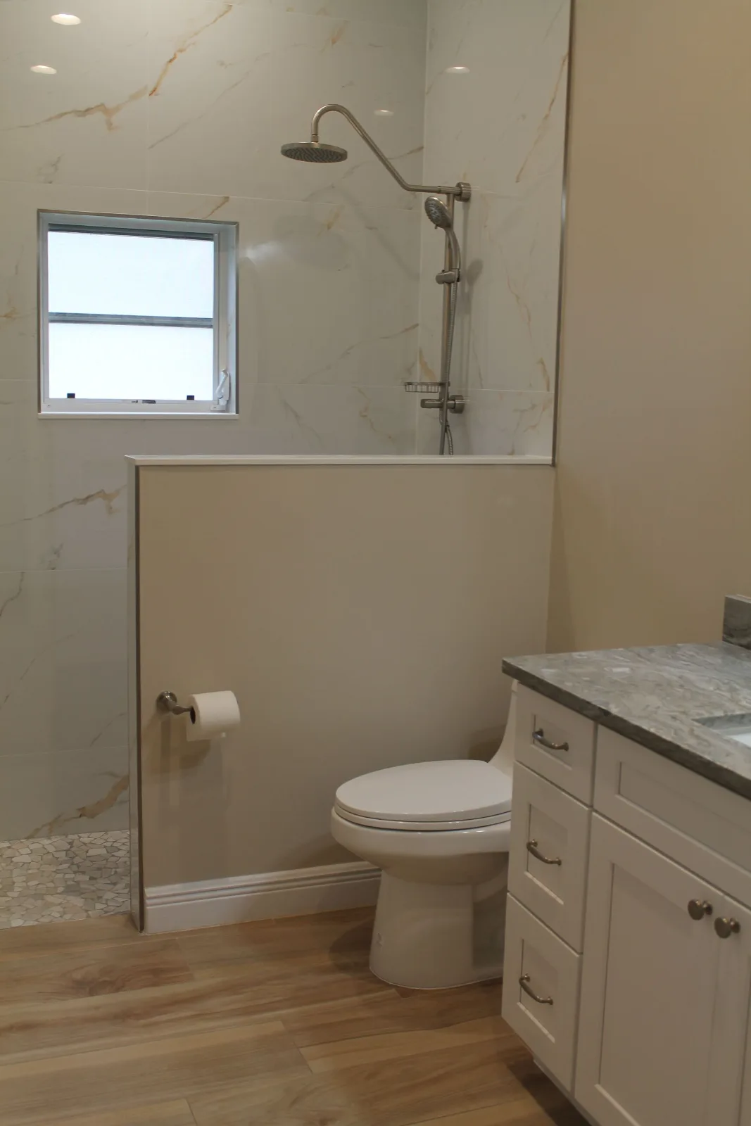 Walk-in shower with a tiled half wall beside a white vanity