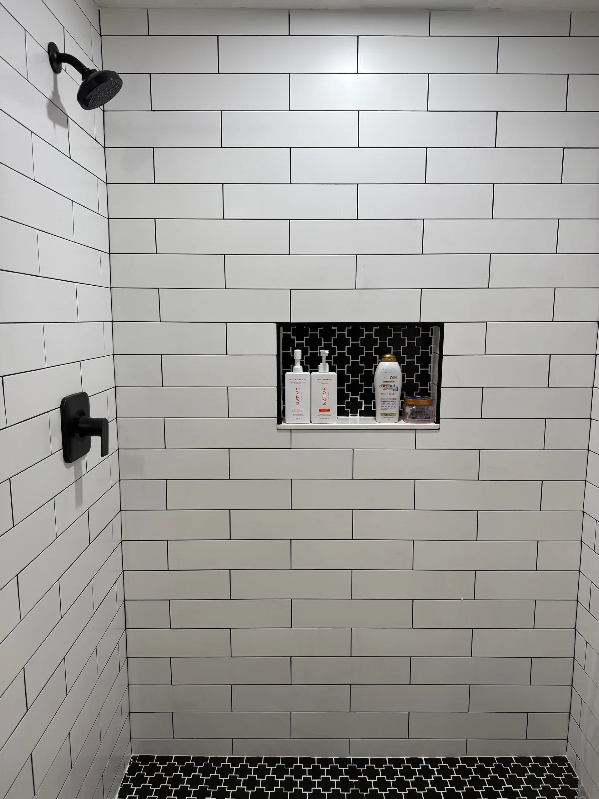White linear tile shower with recessed niche and black hex mosaic floor