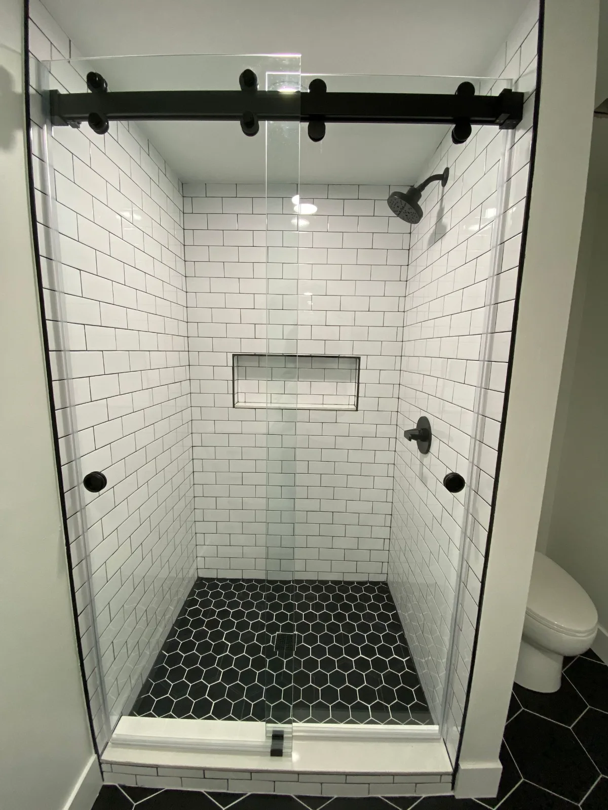 White subway tile shower with a black hexagon mosaic pan