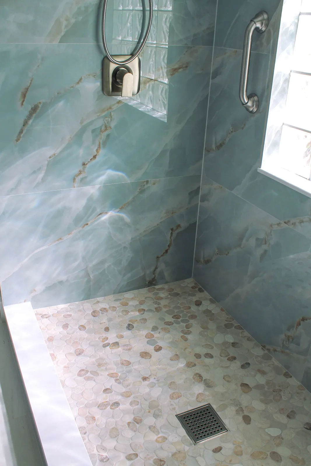 Blue onyx-look walk-in shower with pebble mosaic floor and brushed nickel fixtures