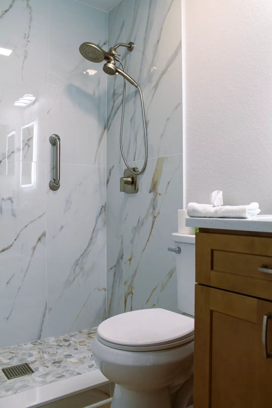 Calacatta-look porcelain shower with grab bar beside an oak vanity