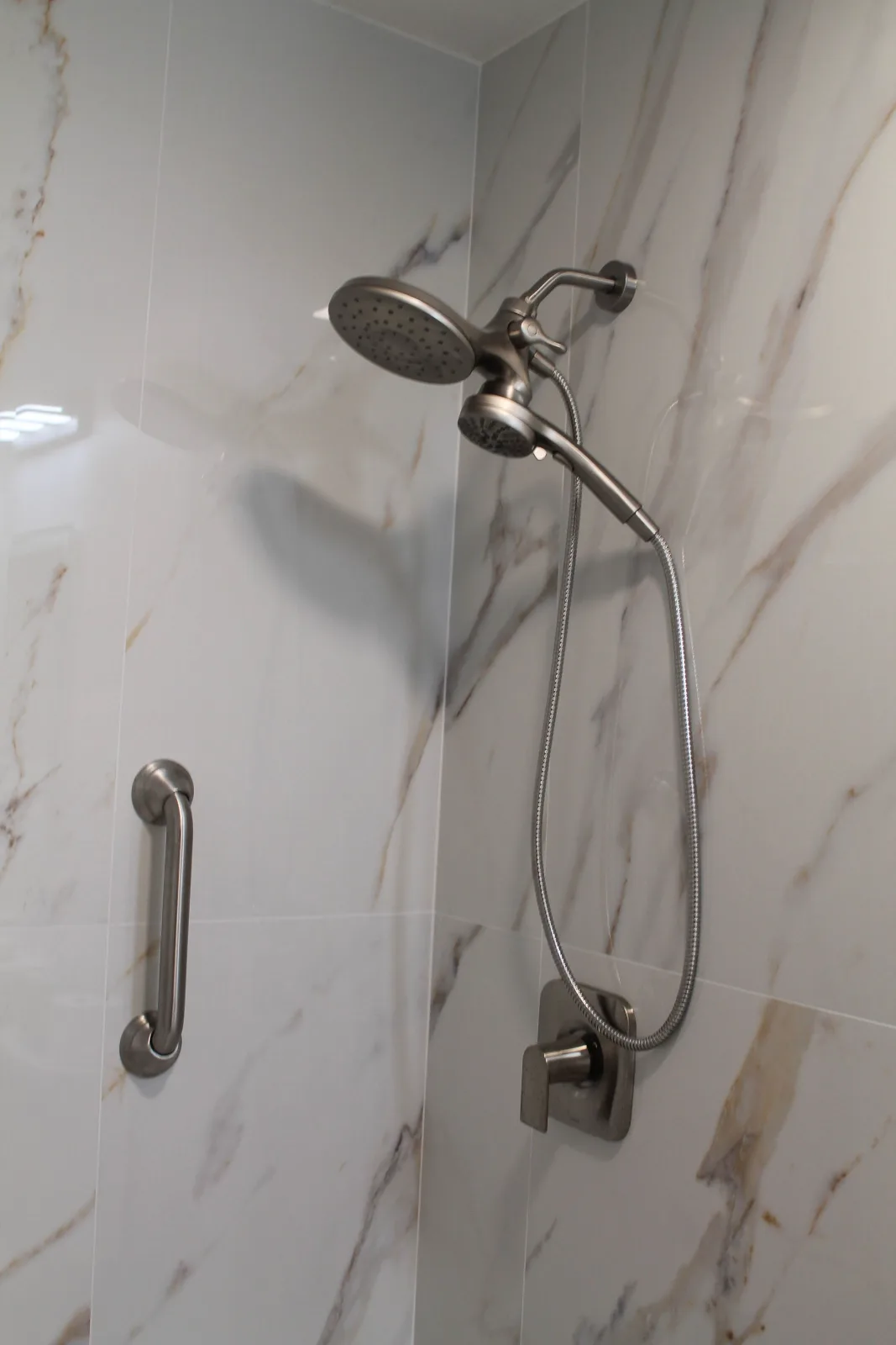 Handheld shower on a slide bar with grab bar on calacatta-look porcelain tile