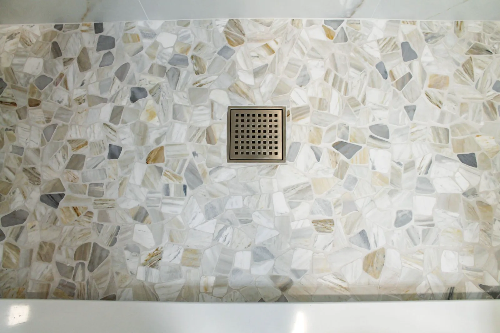 Natural pebble mosaic shower floor with a brushed square drain