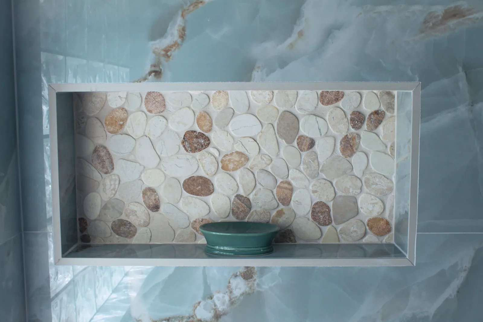 Recessed shower niche lined in pebble mosaic against blue onyx-look tile