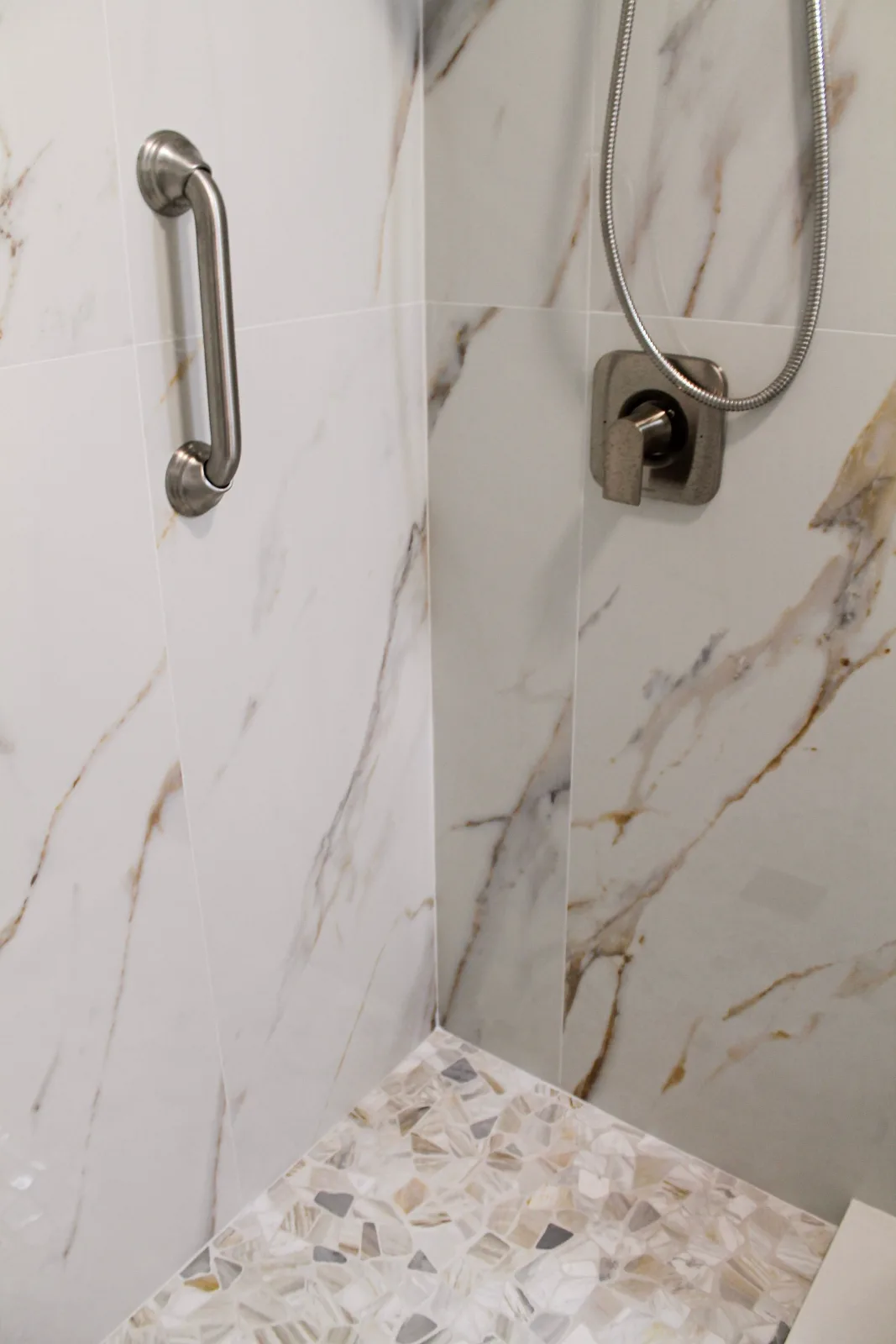 Walk-in shower in calacatta-look tile with pebble mosaic pan and grab bar