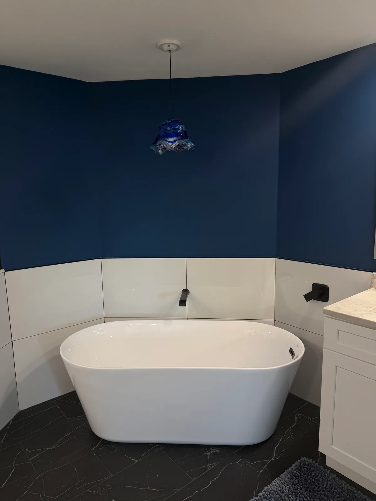Freestanding white soaking tub against a navy accent wall in a Naples master bathroom remodel