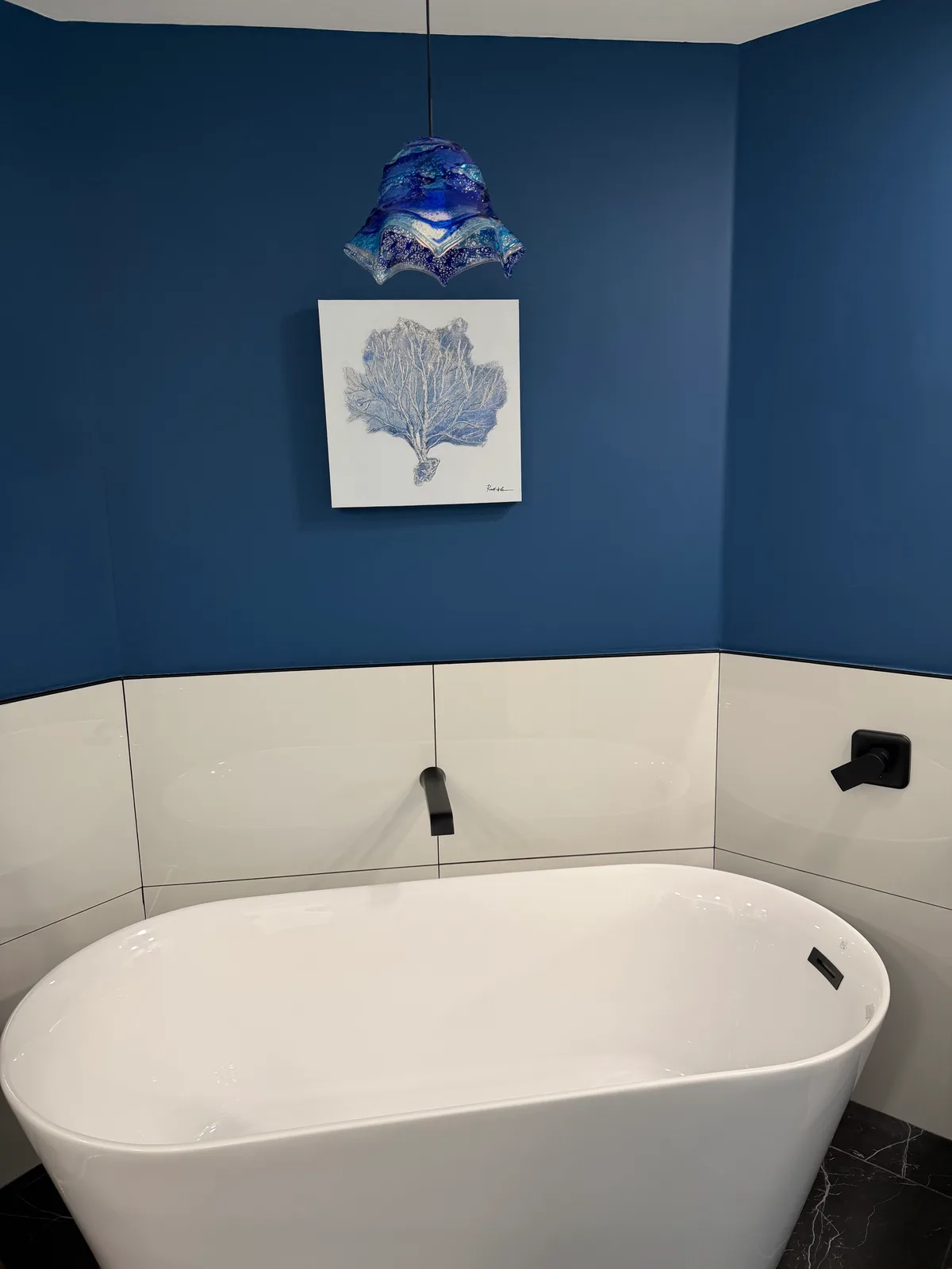 Freestanding tub beneath coastal artwork on a navy feature wall, Naples master bath