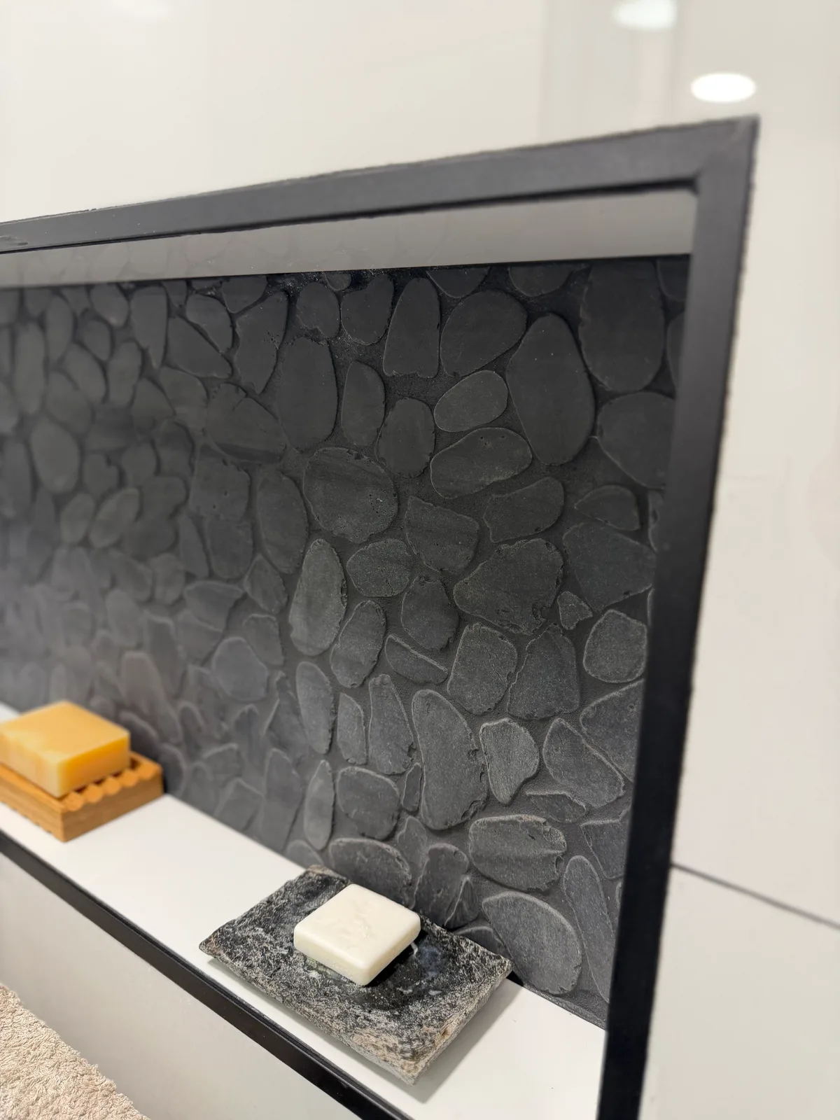 Recessed shower niche backed in grey pebble mosaic against large-format white tile