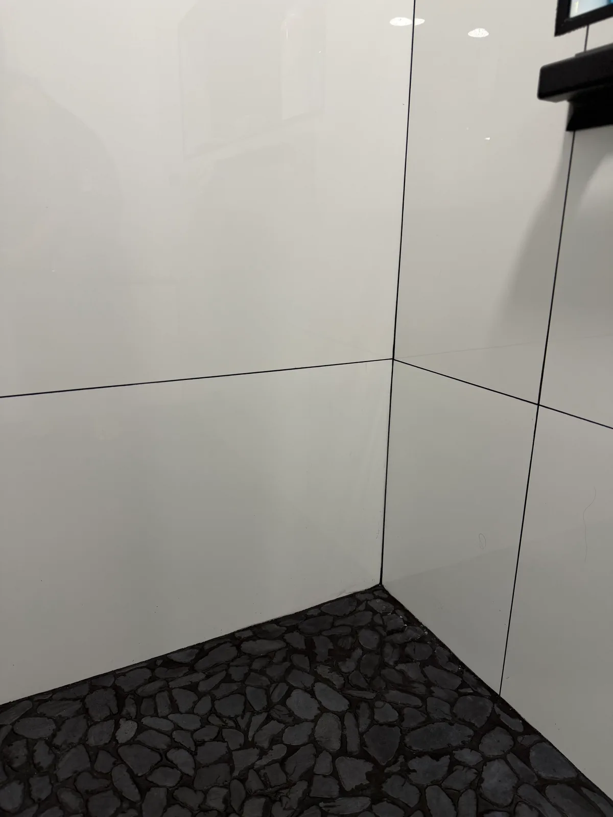 Grey pebble mosaic shower floor against large-format white tile walls, Naples