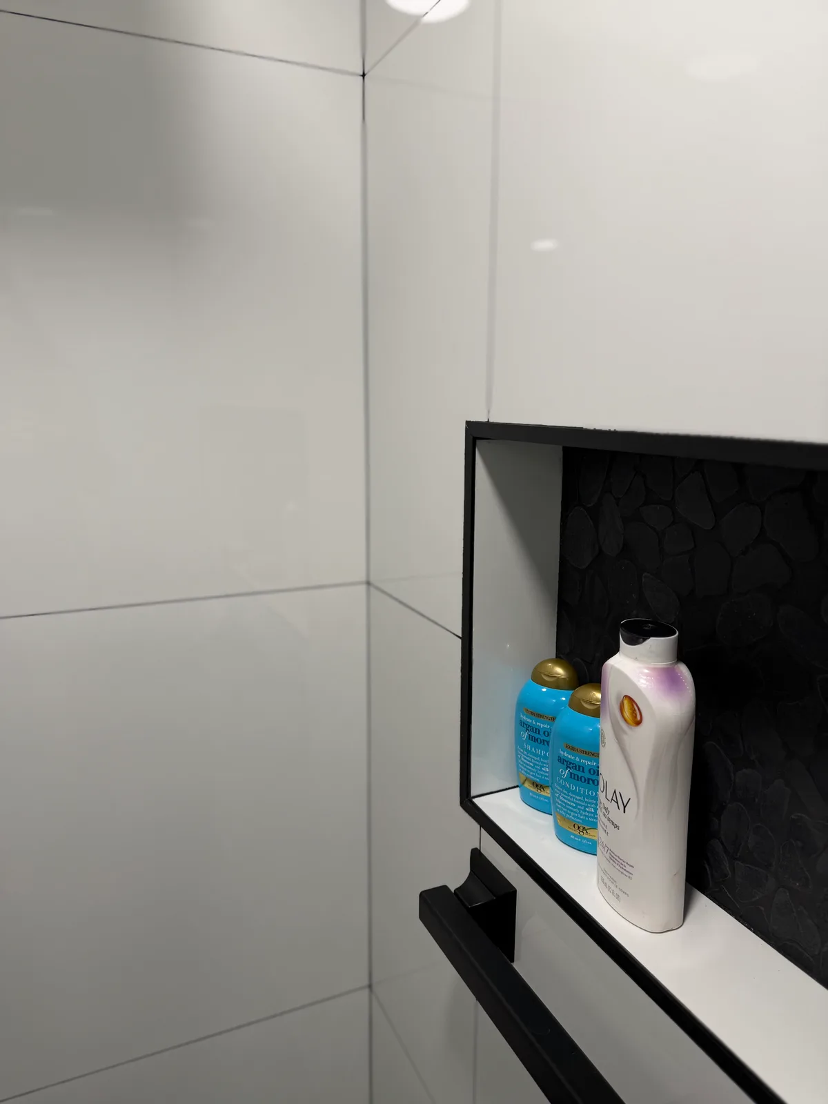 Recessed shower niche with a pebble mosaic back and black trim