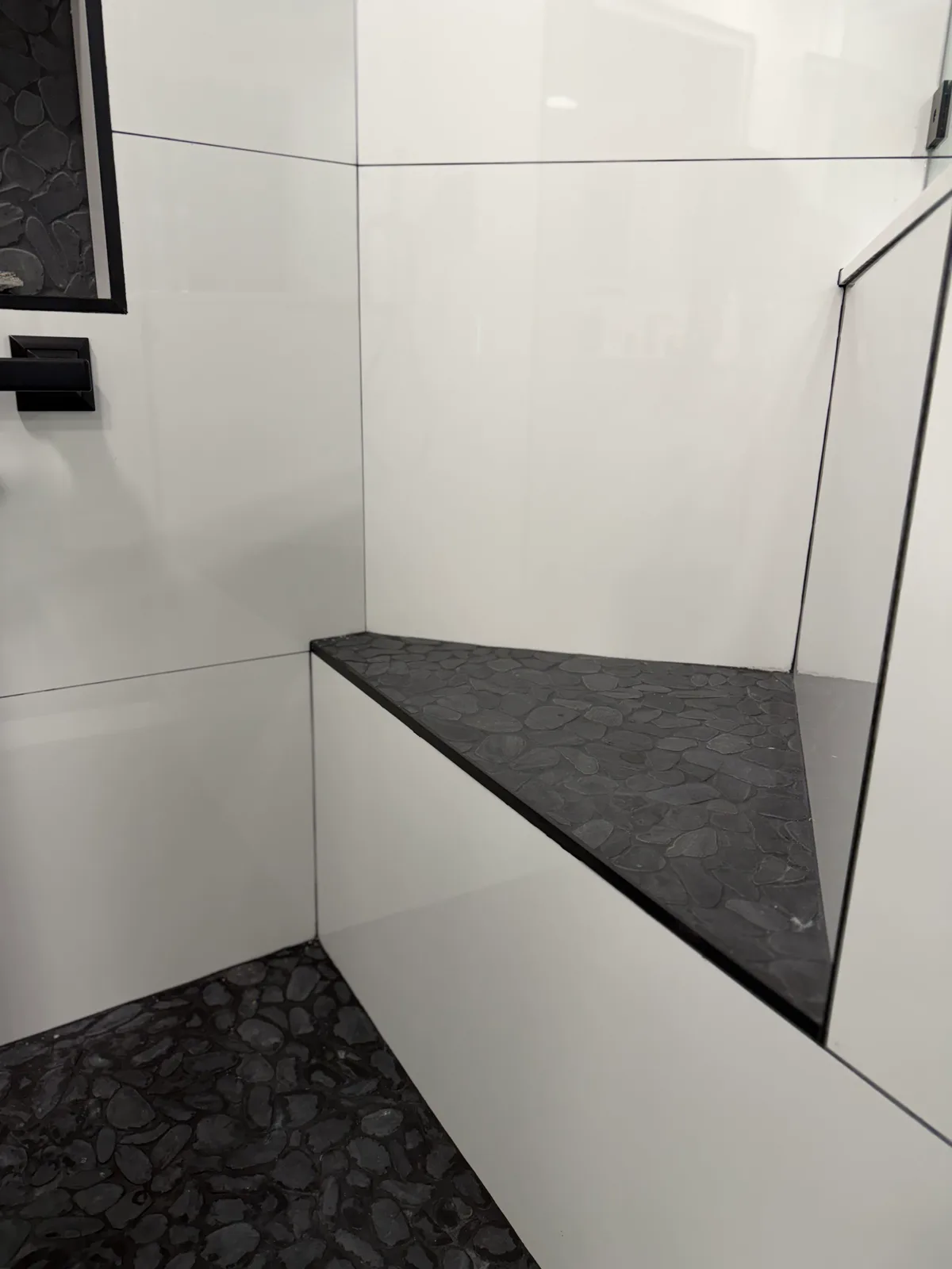 Built-in shower bench with a black stone top beside a frameless glass panel