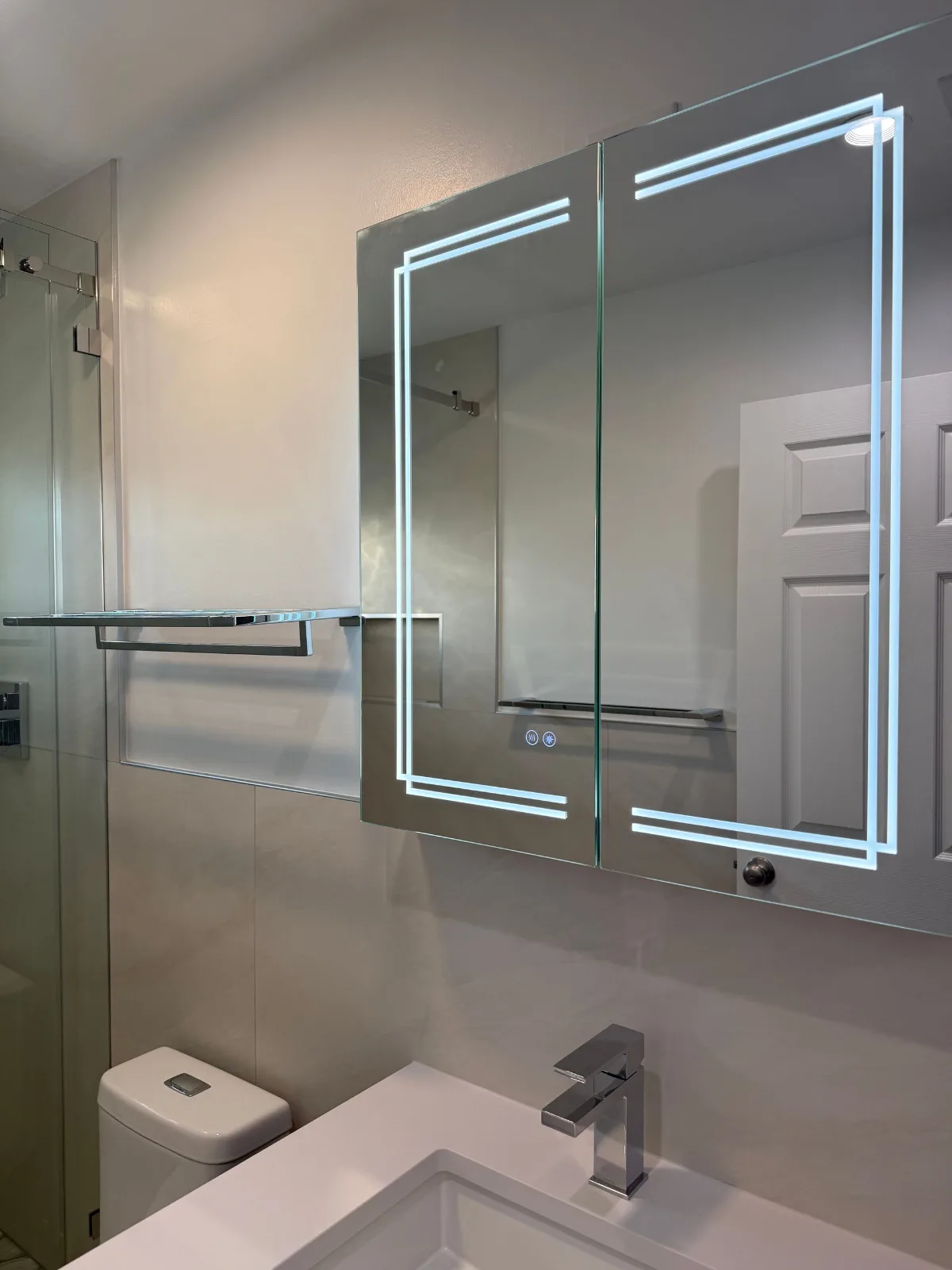 LED-lit medicine cabinet mirror above a quartz vanity with chrome faucet
