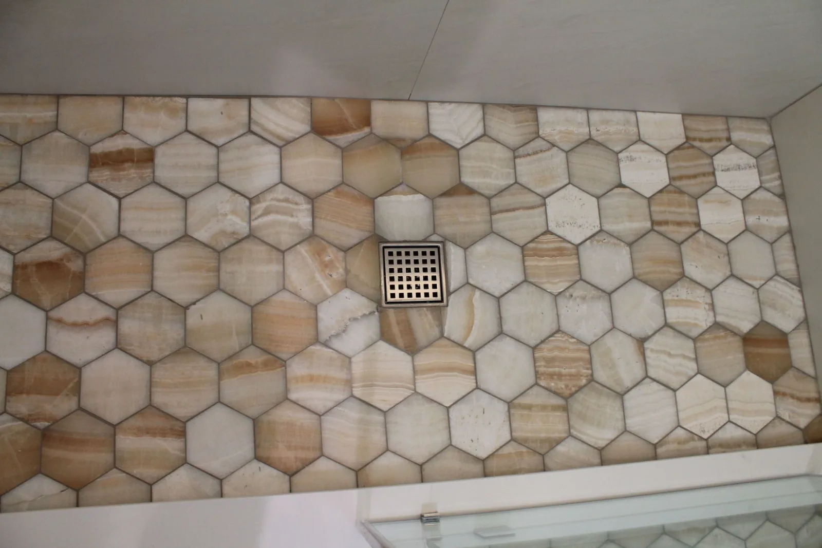 Honey onyx hexagon mosaic shower floor with a stainless square drain
