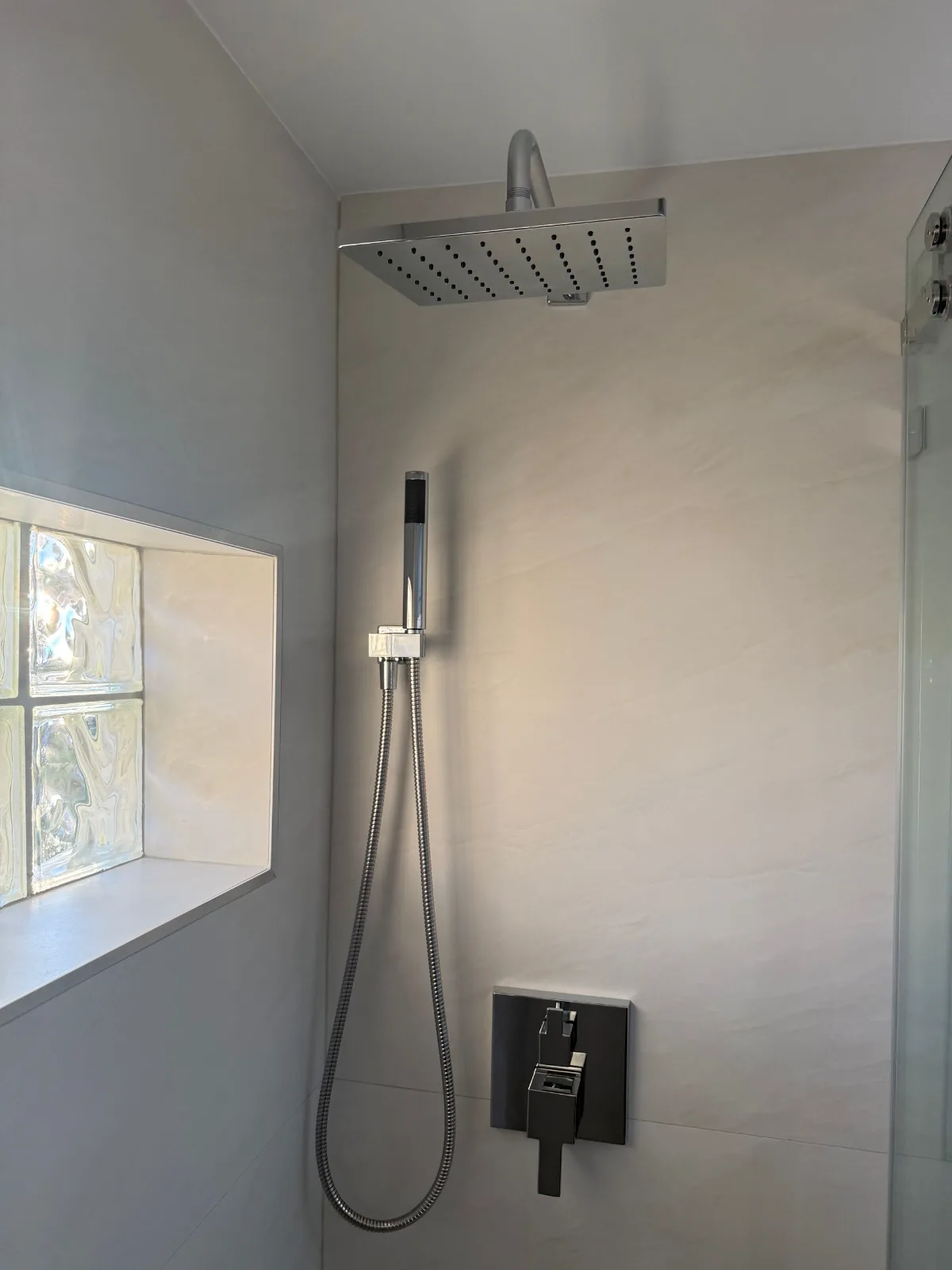 Chrome handheld sprayer beside a glass block shower window