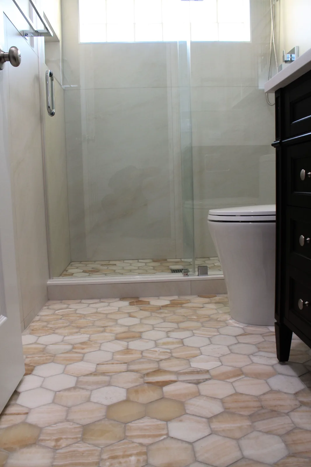 Walk-in shower with honey onyx hex mosaic floor beside an espresso vanity