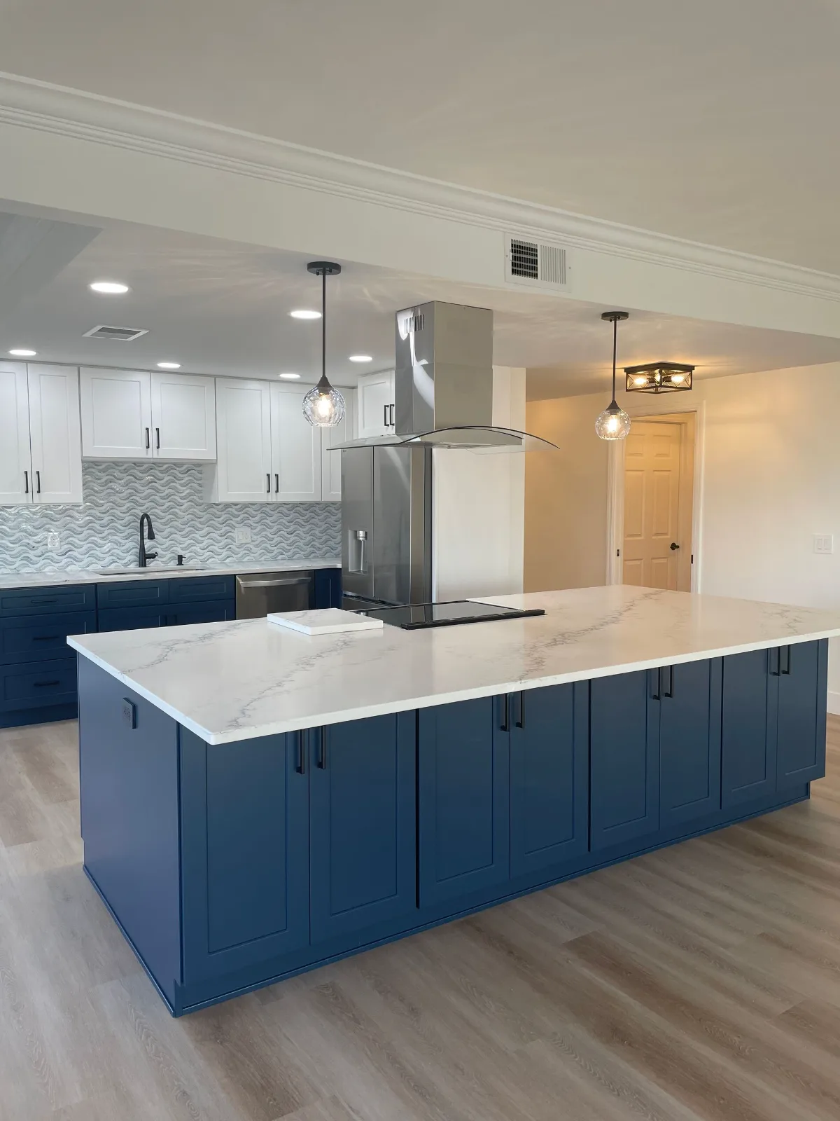 Open-concept kitchen with navy island, white uppers, and luxury vinyl plank flooring