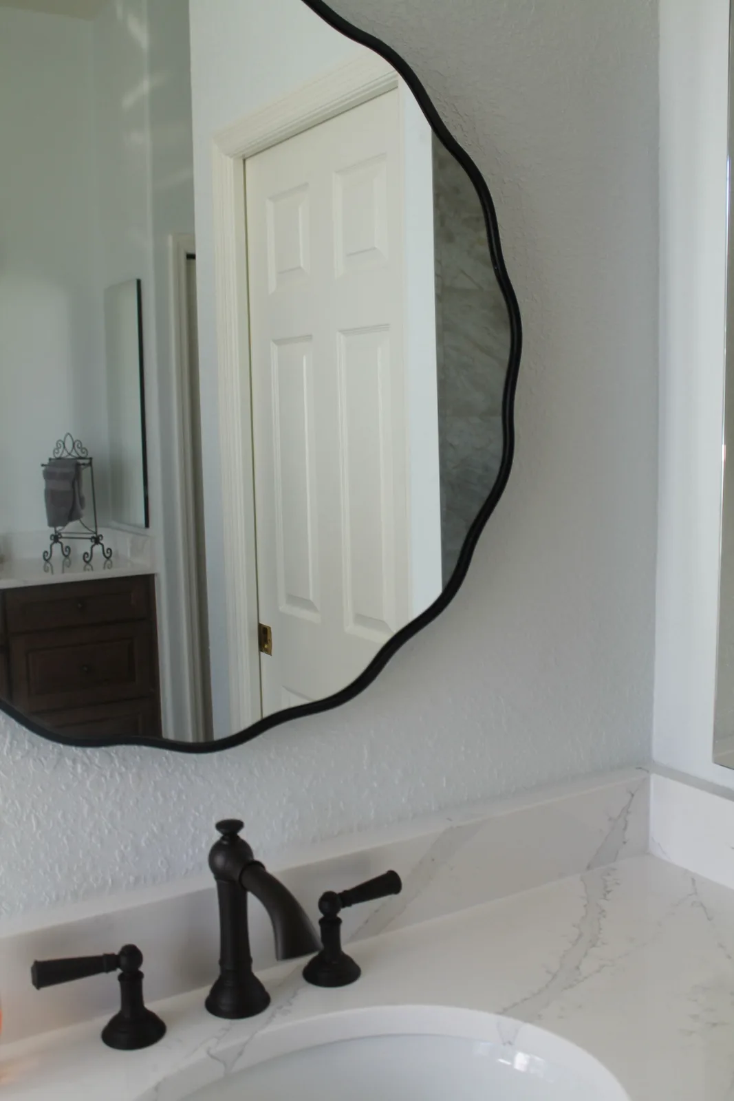 Organic-shaped black mirror above a bronze widespread bathroom faucet