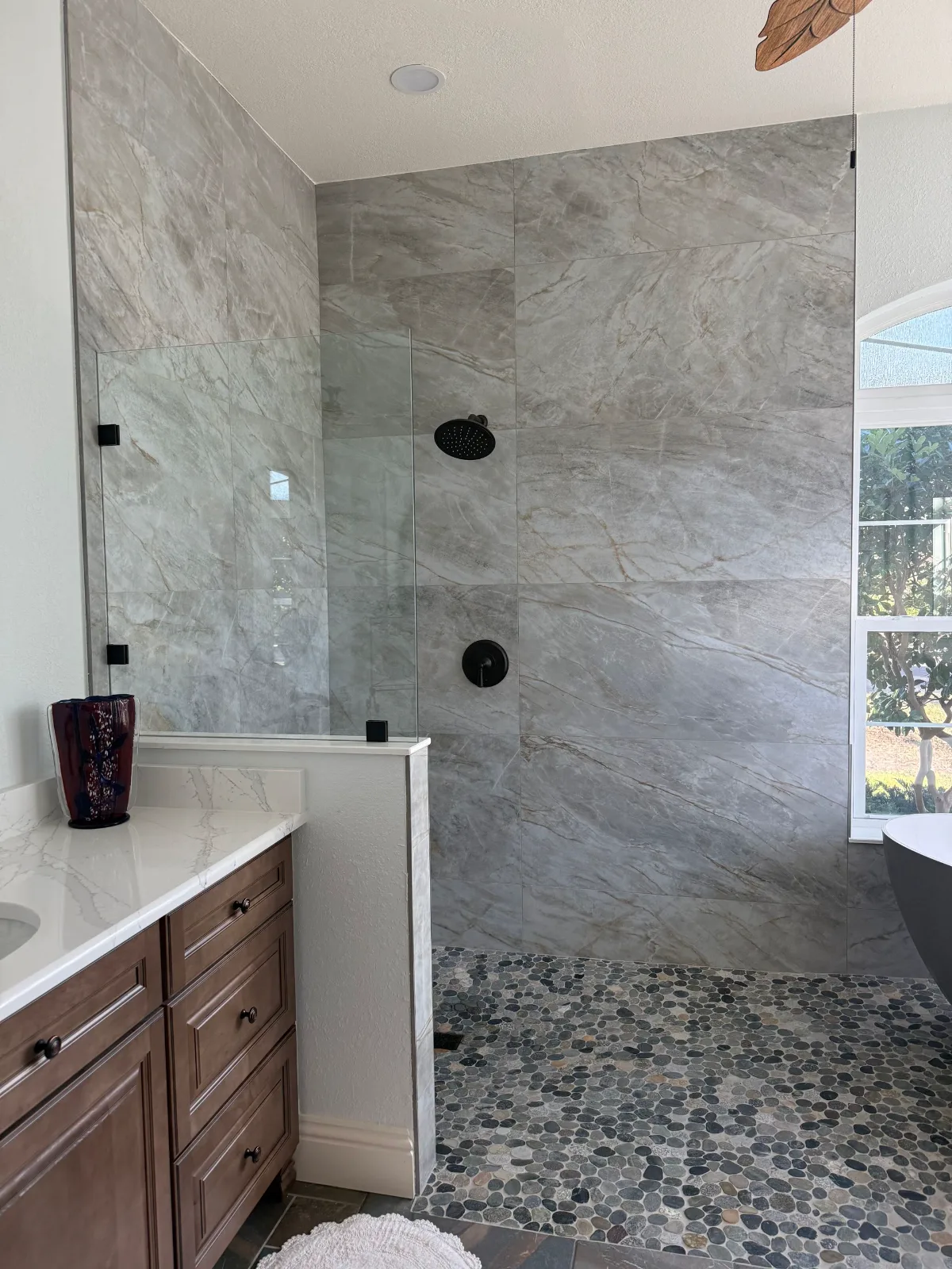 Curbless walk-in shower in quartzite-look porcelain with pebble floor and stained wood vanity