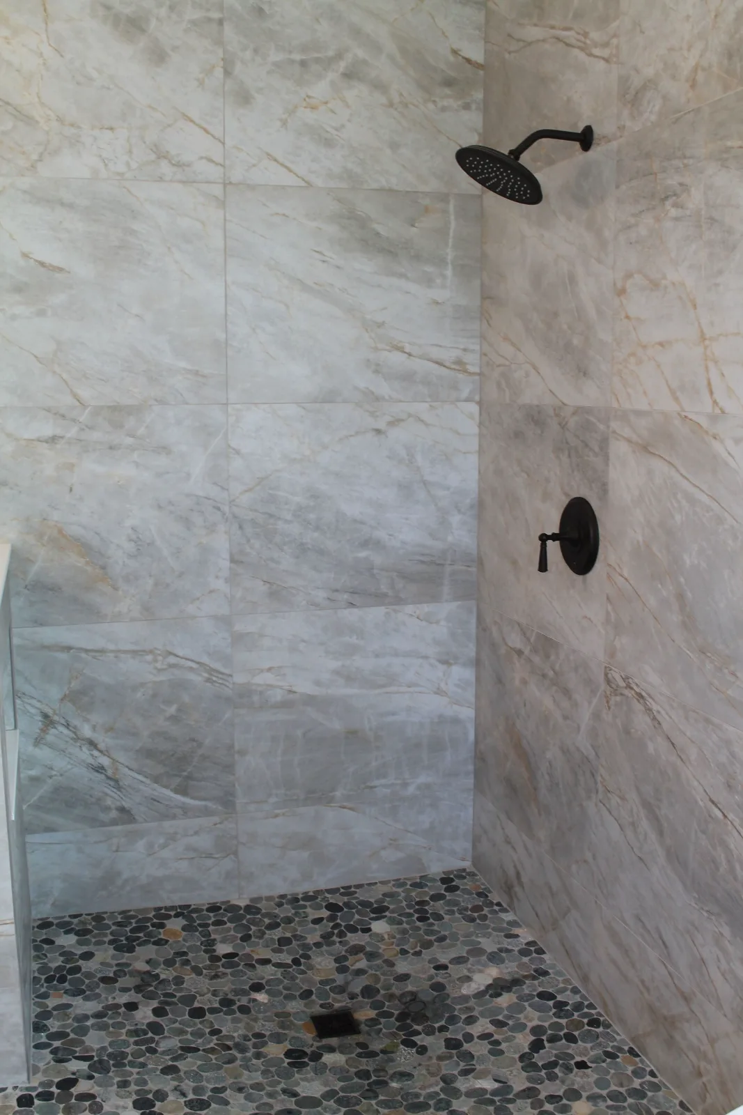 Walk-in shower tiled floor to ceiling in quartzite-look porcelain with a pebble mosaic pan