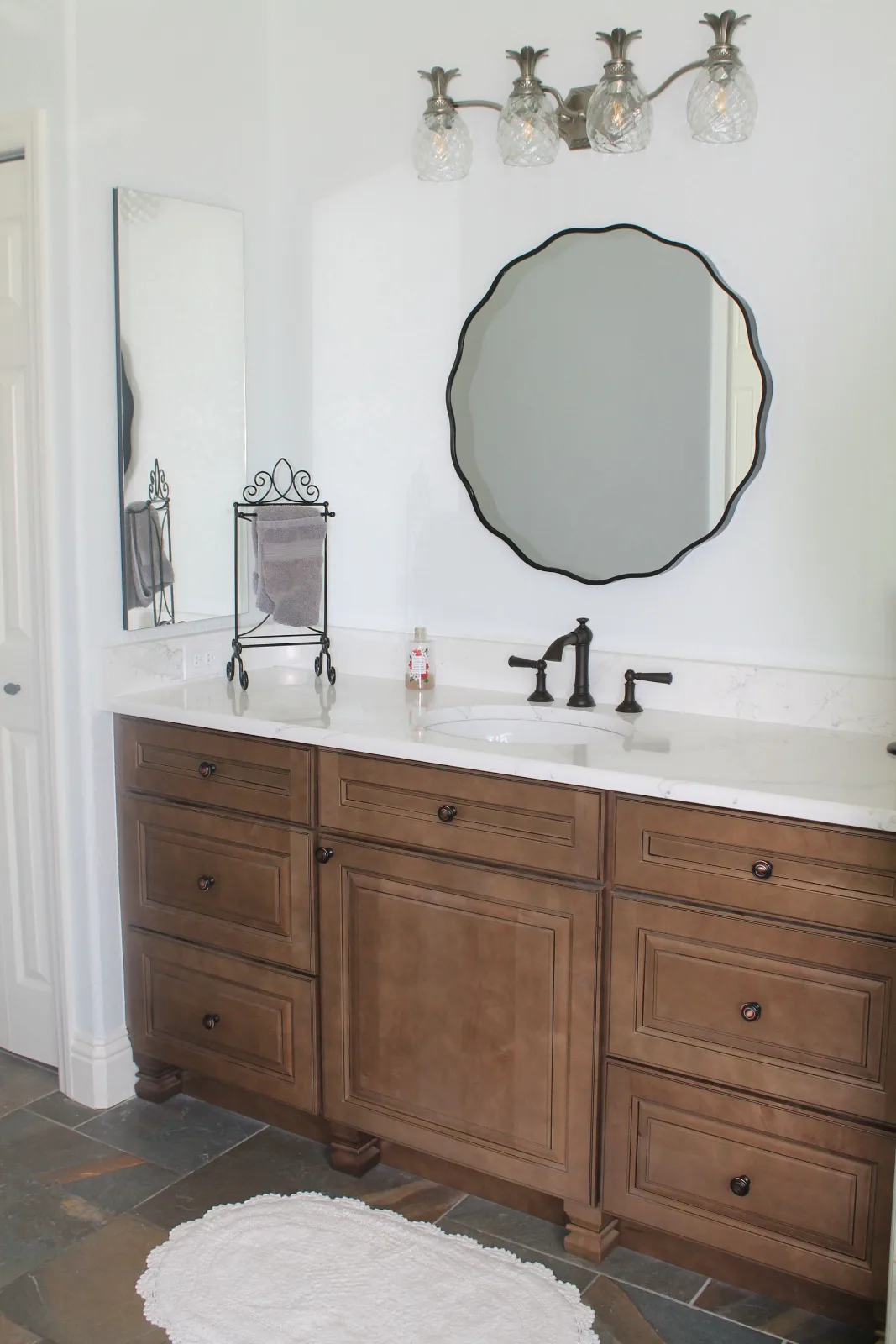 Stained wood shaker vanity with a round black mirror and a bronze faucet