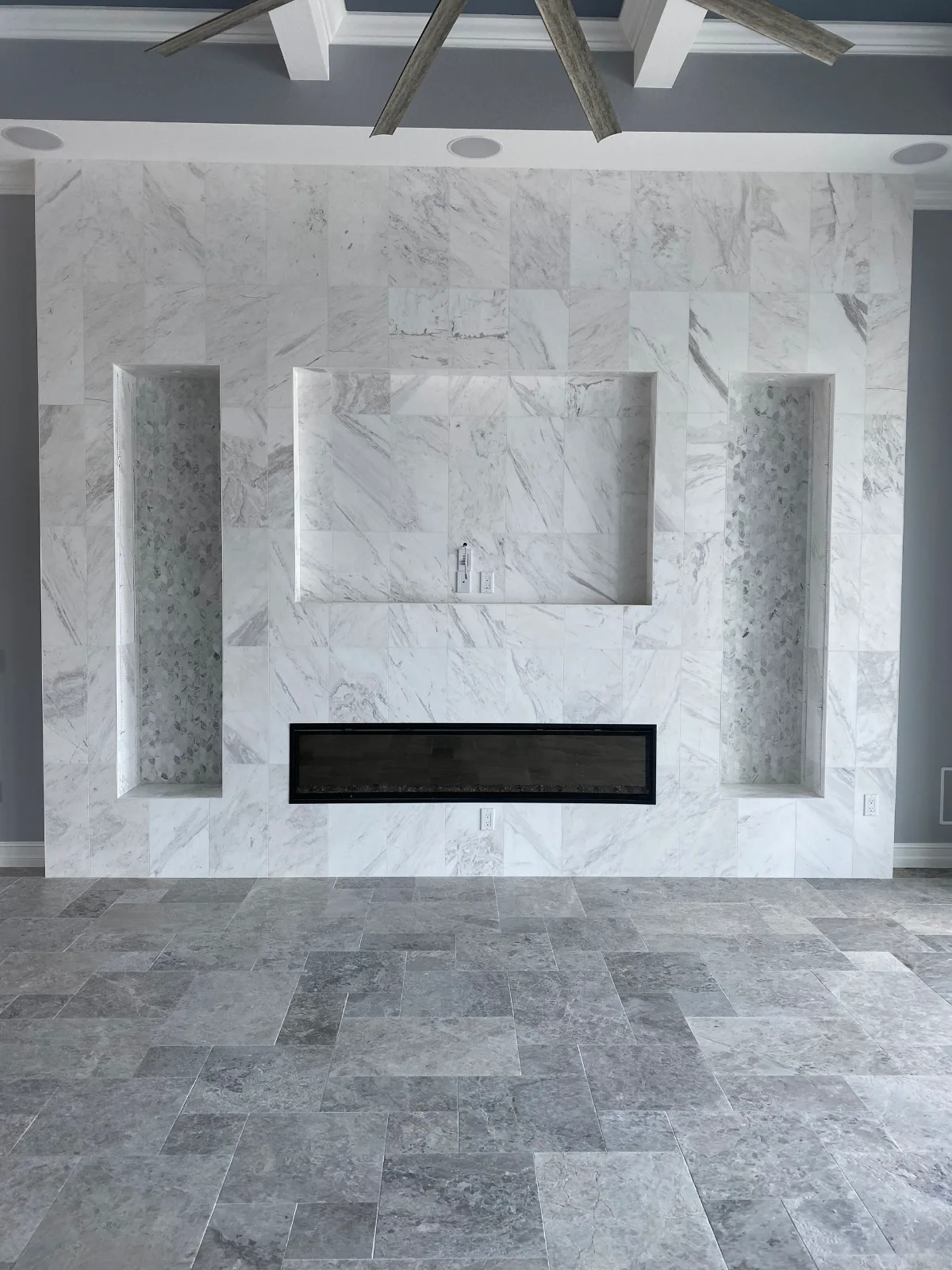Marble tile feature wall with a linear fireplace and recessed display niches in a Southwest Florida great room