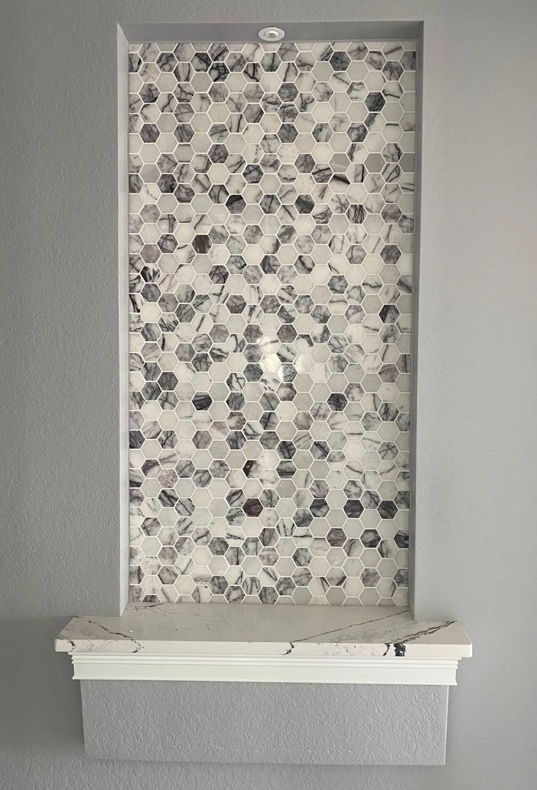 Marble hexagon mosaic accent panel set into a tiled wall niche