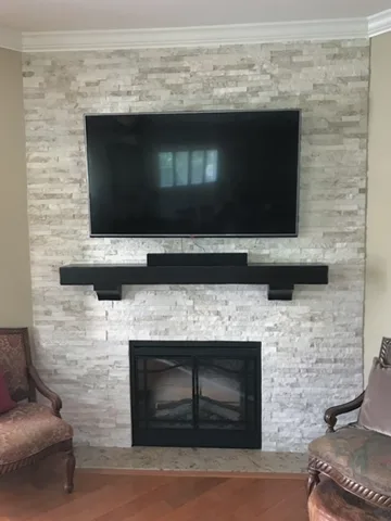 Floor-to-ceiling stacked stone fireplace wall with a wall-mounted TV and a black timber mantel