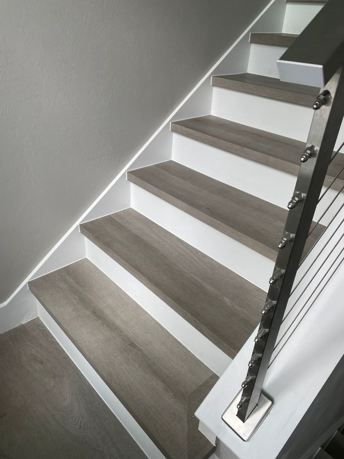 Grey vinyl plank stair treads with white risers beside a stainless cable railing