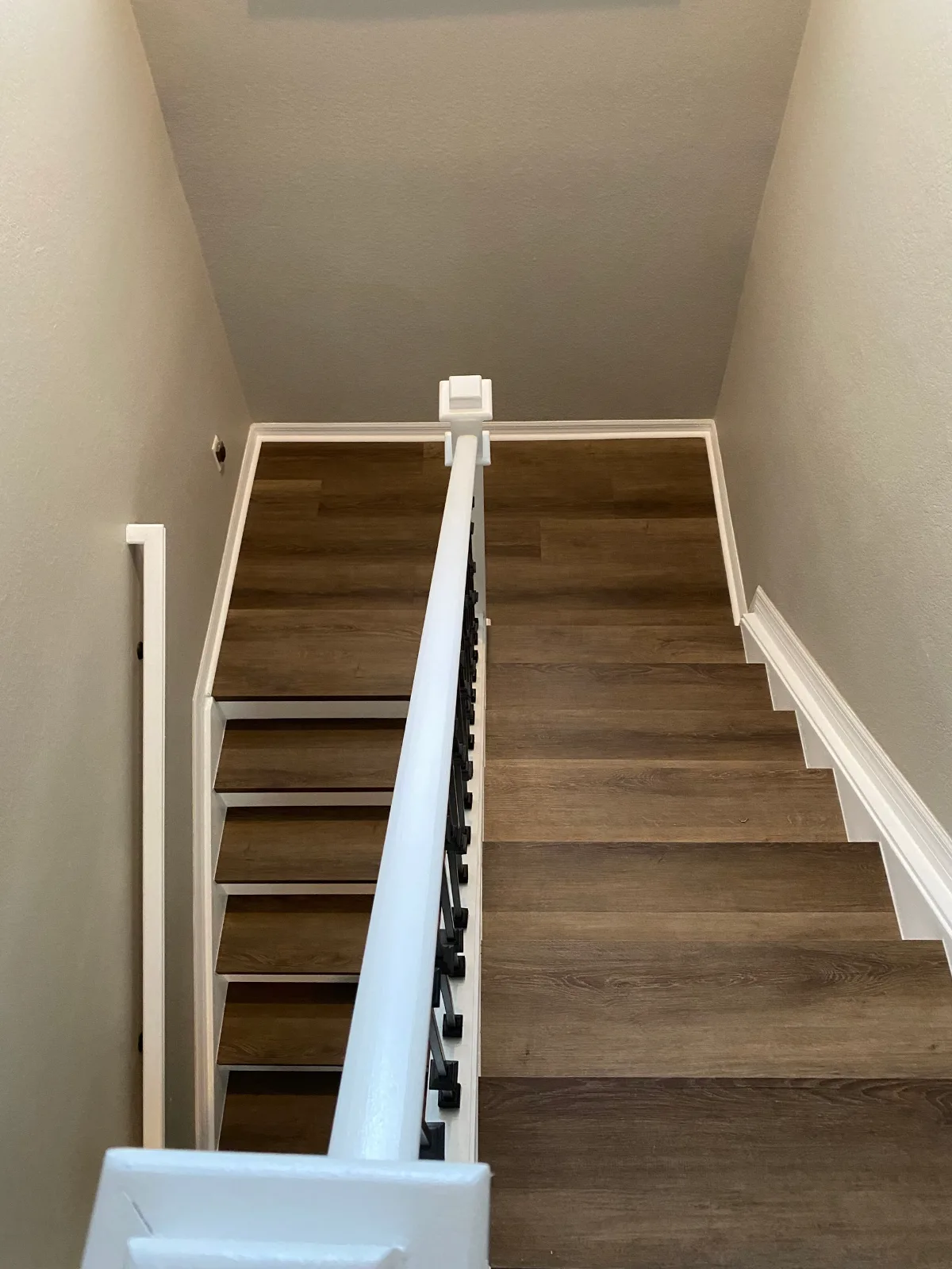 Walnut wood-look vinyl plank stair treads with white risers and a black railing
