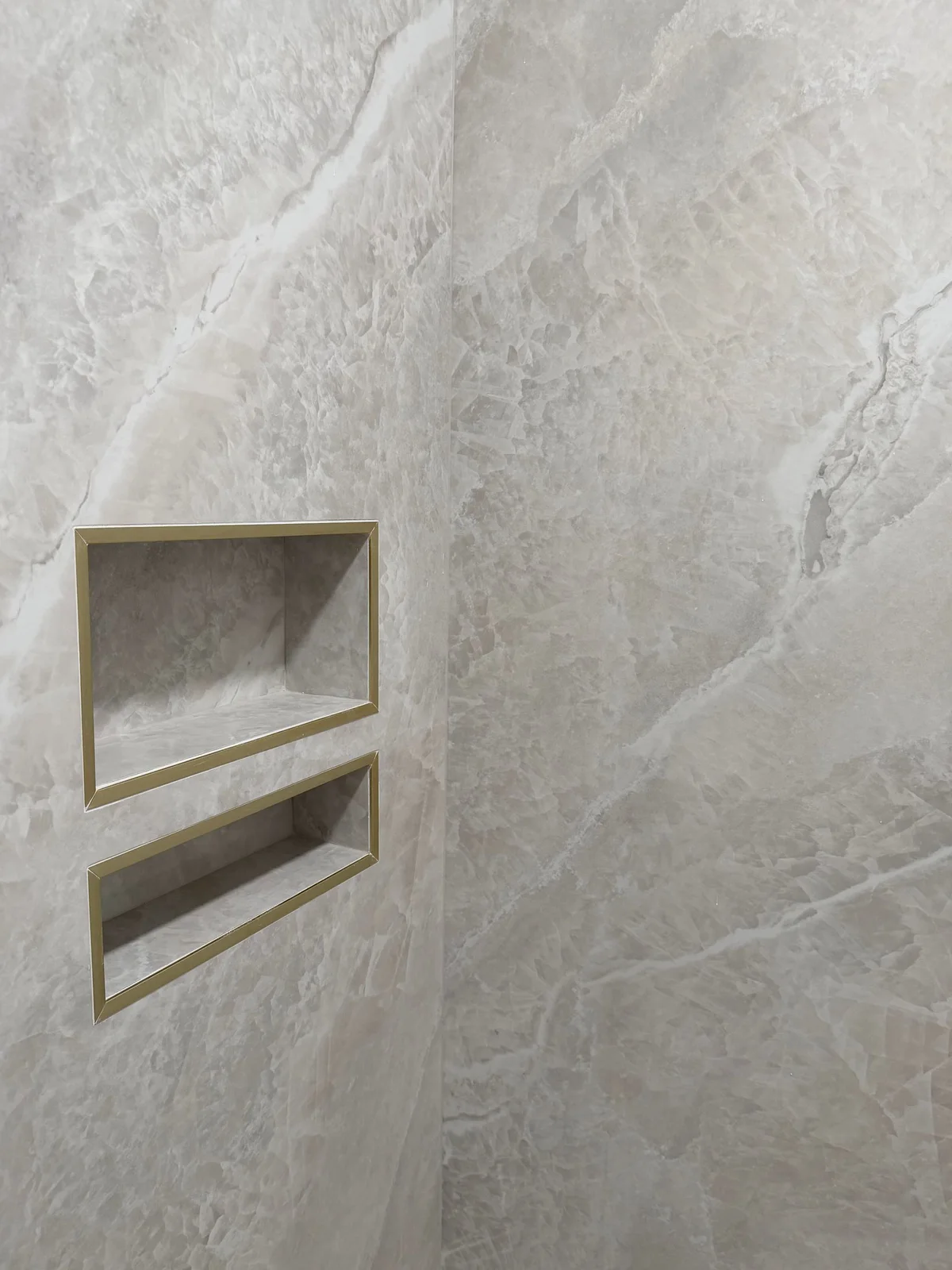 Two stacked recessed shower niches trimmed in brushed gold against quartzite-look porcelain wall tile